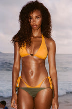 Woman wearing a yellow bikini standing on a beach with ocean in the background